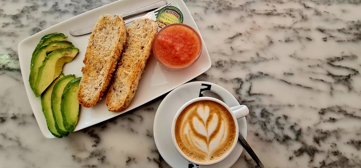 Desayuno completo con pan tostado, aguacate, mermelada y café con arte latte
